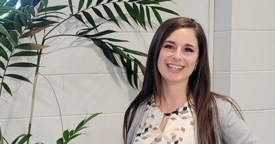 Sharleena Wilson, Relationship Manager at Safety 'n Action, smiling and standing in front of a white wall and indoor plant, wearing a patterned blouse and black skirt.