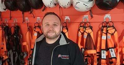 Christopher Petitpas smiling in front of the height safety harness and helmet wall at the Safety 'n Action Tauranga training centre.