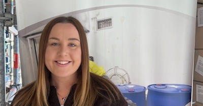 Ailish Thompson smiling in front of a Safety 'n Action pull-up banner promoting real workplace training.