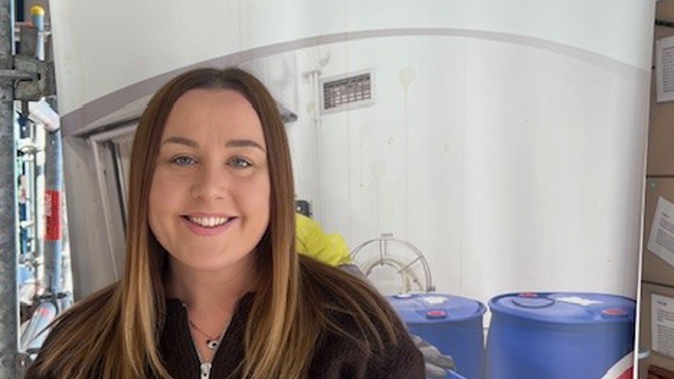 Ailish Thompson smiling in front of a Safety 'n Action pull-up banner promoting real workplace training.