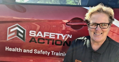 Ginny Kamphaug smiling beside a red Safety 'n Action vehicle displaying the Health and Safety Training logo.